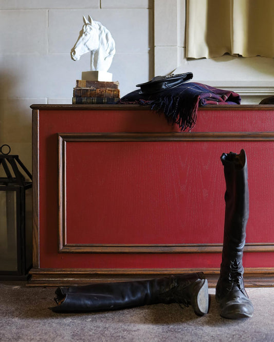 Red sideboard with a horse statue, books, and a coat, with boots on the floor.