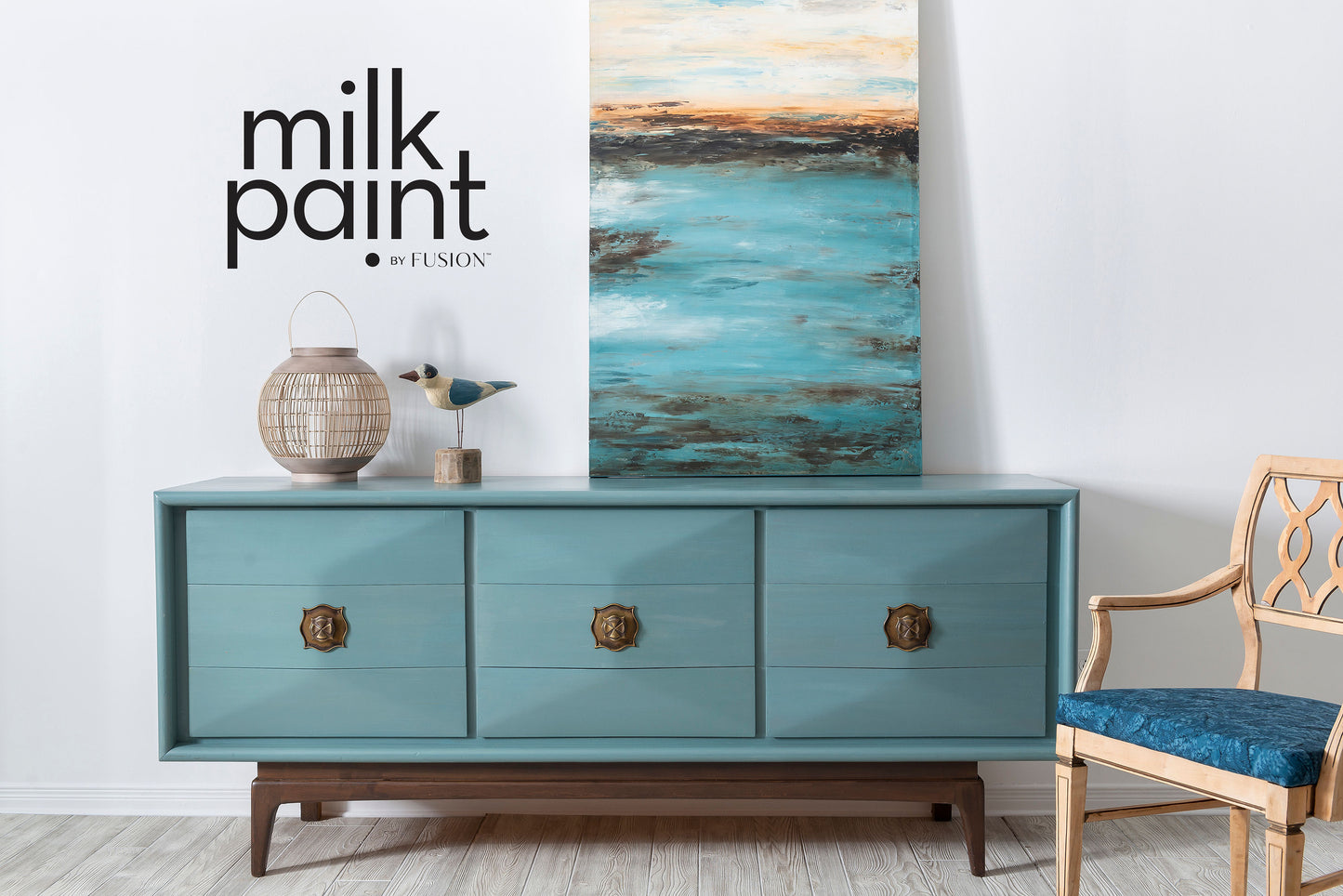 Teal dresser with gold knobs in a room with a chair and abstract painting.