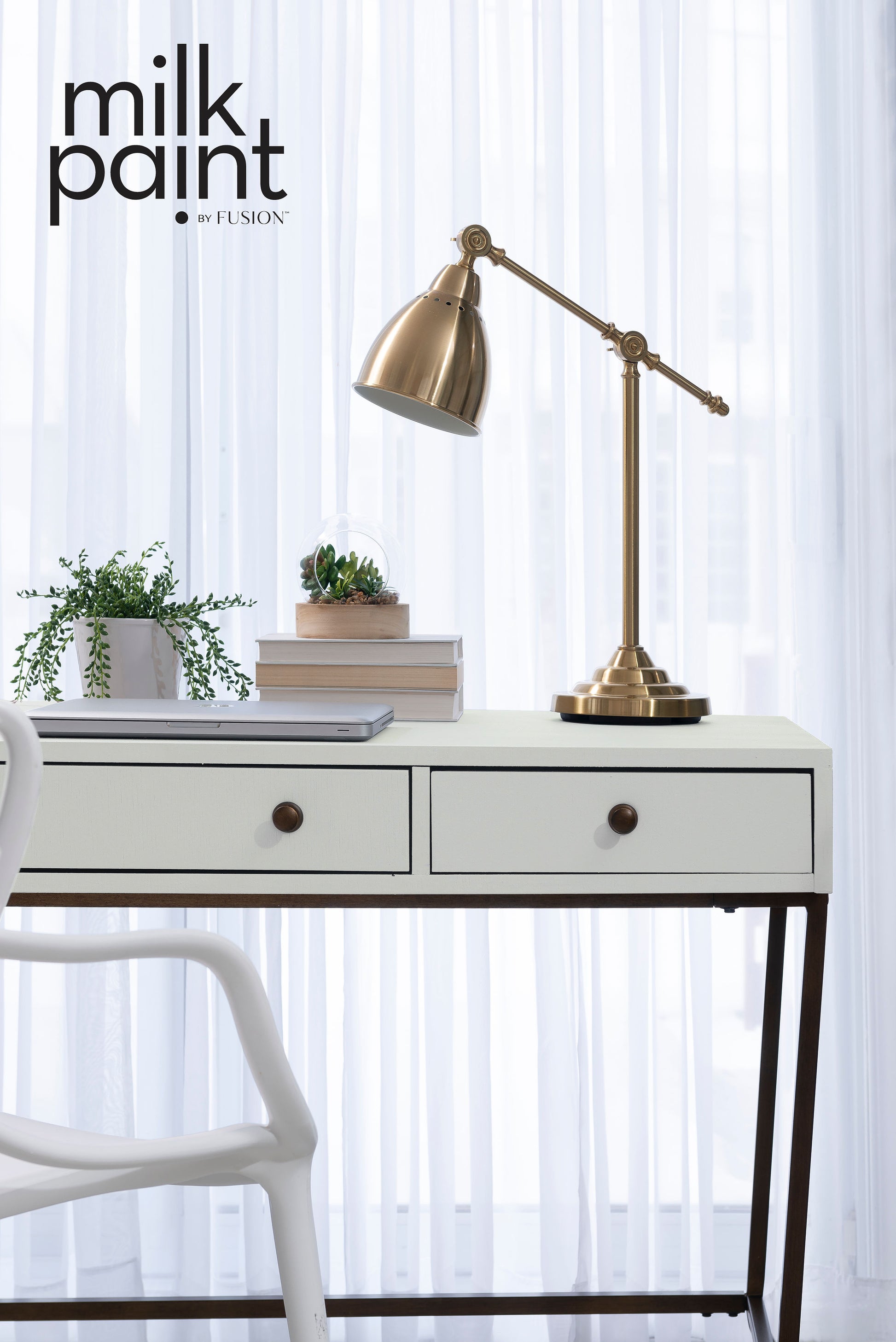 White desk with a gold lamp and books against a white curtain background, featuring the Fusion Milk Paint logo.