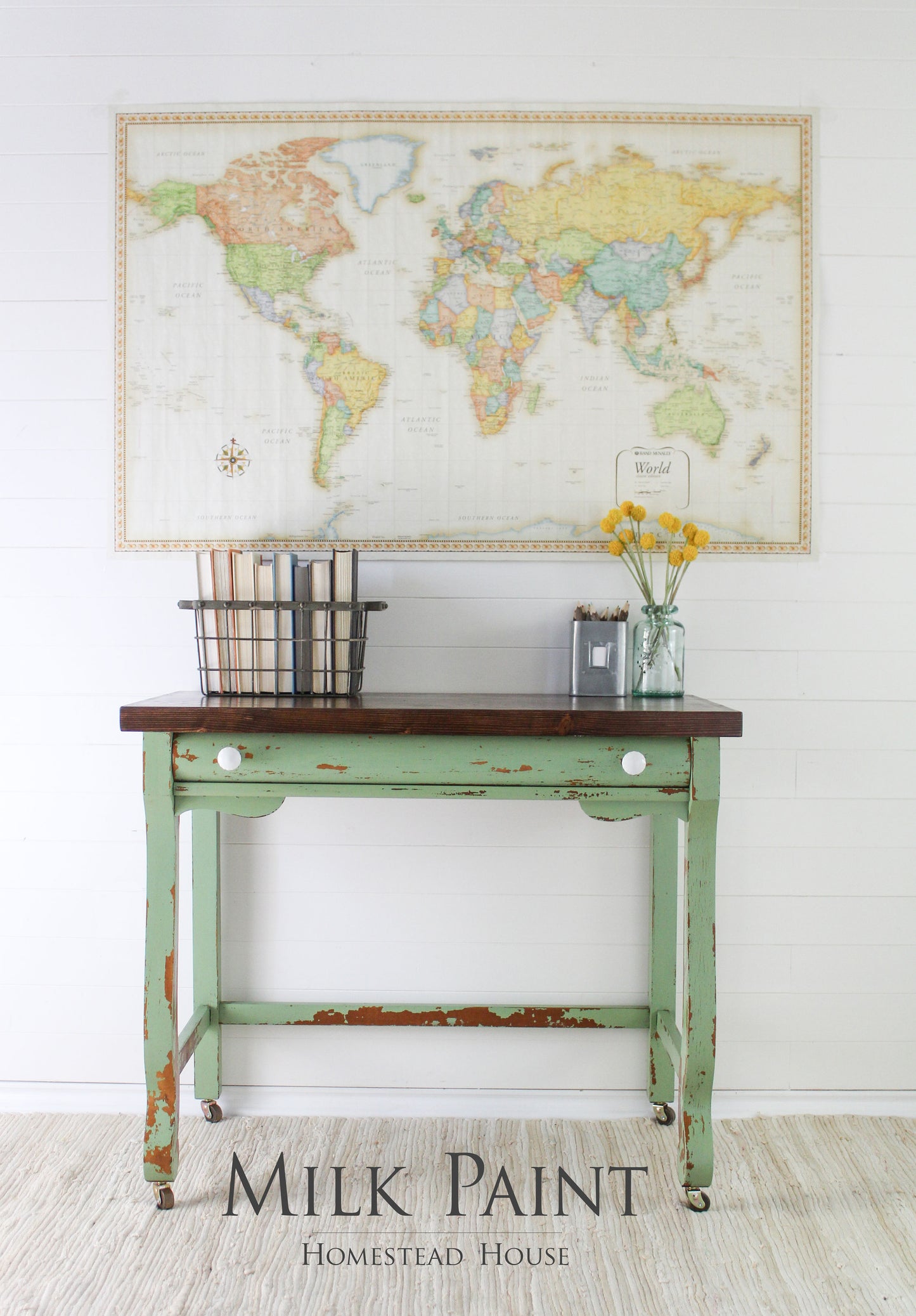 Vintage-style table with world map and decor items against a white wall, featuring 'Milk Paint' branding.