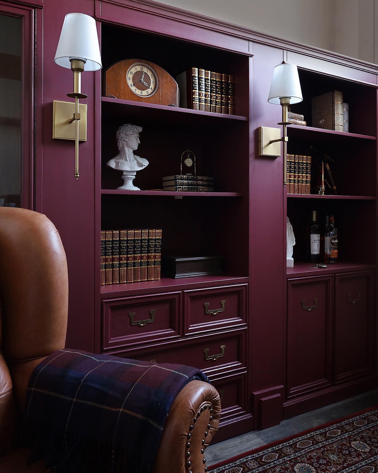 Mauve bookshelf with decorative items in a room with a leather chair.