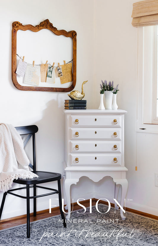 White dresser with gold knobs in a room with a mirror and chair, featuring Fusion Mineral Paint branding.