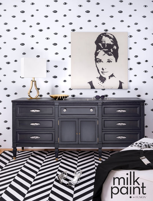 Black dresser against a patterned wall with a portrait above it, featuring 'milk paint' branding.