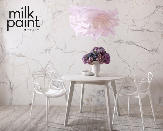 Dining area with a table and chairs against a marble wall, featuring 'milk paint' branding.