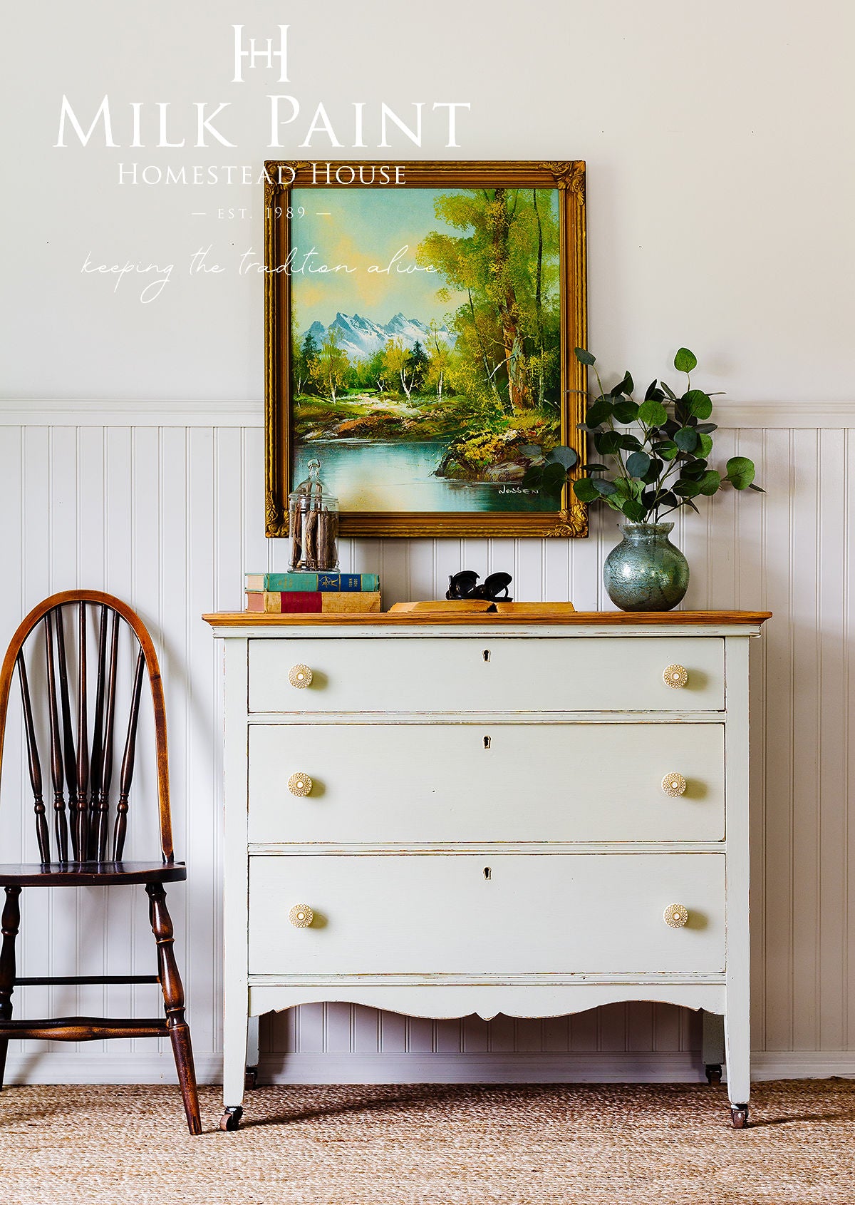 White dresser with gold accents, framed painting, and decorative items against a white wall.